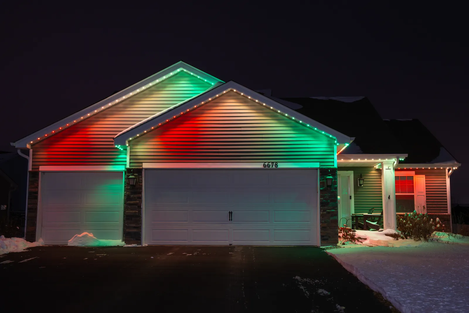 A ranch home in snow lit in alternating red and green along the gables and eaves.